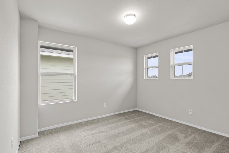 Image of a bedroom with cream walls. tan carpeting, windows, and white trim