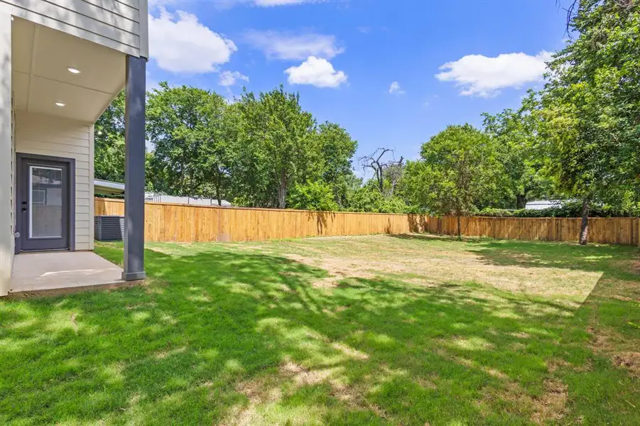 Expansive rear yard featuring a wooden privacy fence, mature trees, and a concrete patio beneath a covered porch Expansive rear yard featuring a wooden privacy fence, mature trees, and a concrete patio beneath a covered porch