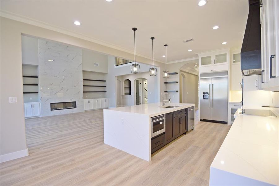 Kitchen featuring sink, a kitchen island with sink, a fireplace, white cabinets, and appliances with stainless steel finishes