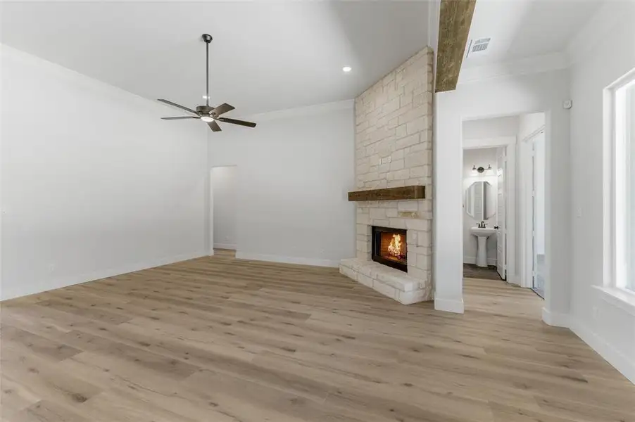 Unfurnished living room with a stone fireplace, ceiling fan, ornamental molding, light wood-style flooring, and recessed lighting