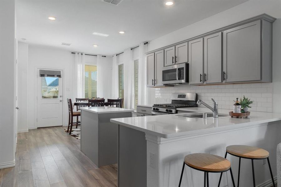 Kitchen with gray cabinetry, sink, light wood-type flooring, appliances with stainless steel finishes, and kitchen peninsula