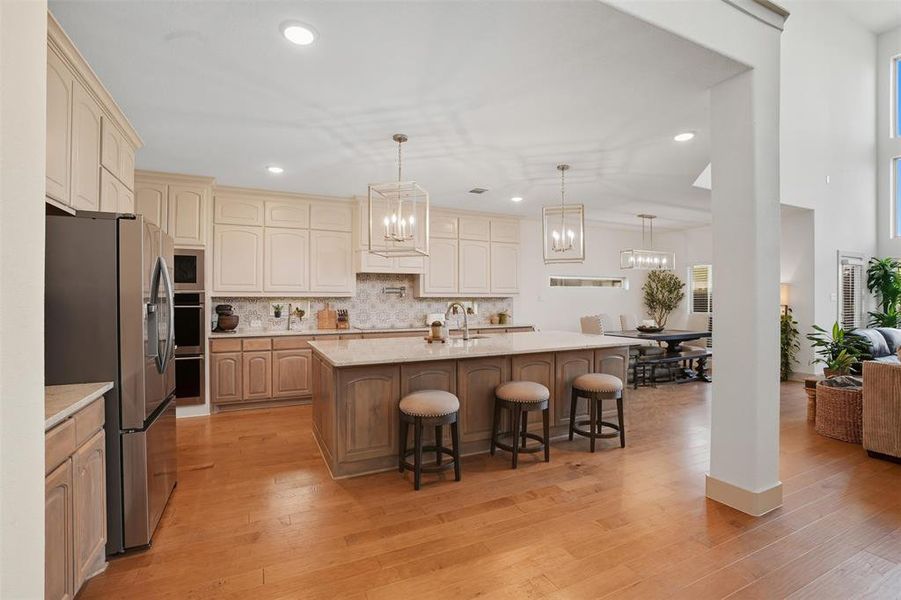 Kitchen featuring hanging light fixtures, appliances with stainless steel finishes, tasteful backsplash, a center island with sink, and light stone counters Kitchen featuring hanging light fixtures, appliances with stainless steel finishes, tasteful backsplash, a center island with sink, and light stone counters