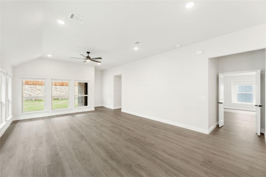 Open living room with vaulted ceiling, ceiling fan, hardwood floors, and large windows overlooking backyard Open living room with vaulted ceiling, ceiling fan, hardwood floors, and large windows overlooking backyard