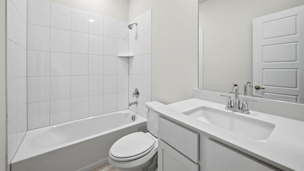 Bathroom featuring a white vanity with an integrated sink and chrome faucet, a large wall mirror, a white panel door, and a shower-over-tub combination with white subway tile surround and a built-in shelf Bathroom featuring a white vanity with an integrated sink and chrome faucet, a large wall mirror, a white panel door, and a shower-over-tub combination with white subway tile surround and a built-in shelf
