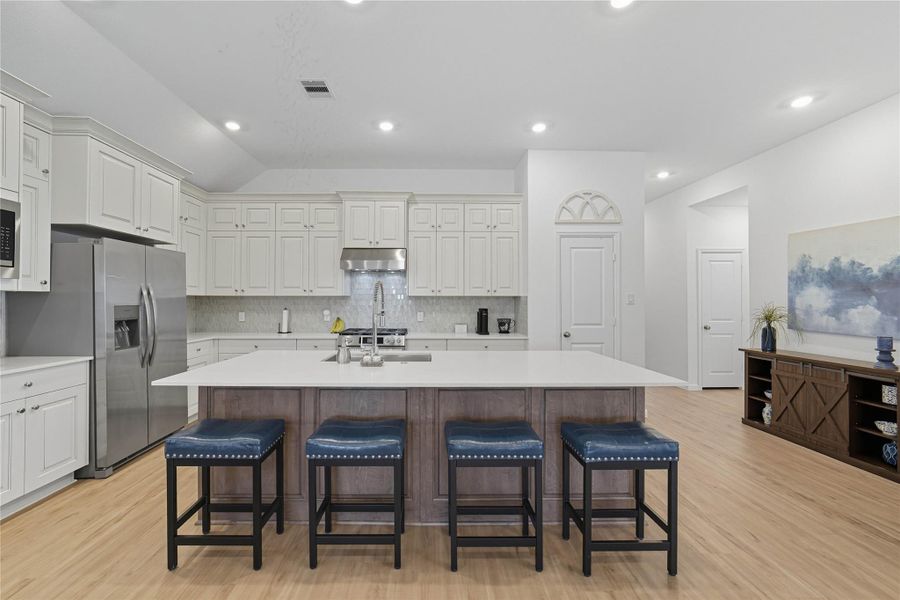 The kitchen features an abundance of cabinetry and a spacious island with seating. The open layout is complemented by light wood-look flooring and recessed lighting, creating a bright and inviting space. The kitchen features an abundance of cabinetry and a spacious island with seating. The open layout is complemented by light wood-look flooring and recessed lighting, creating a bright and inviting space.