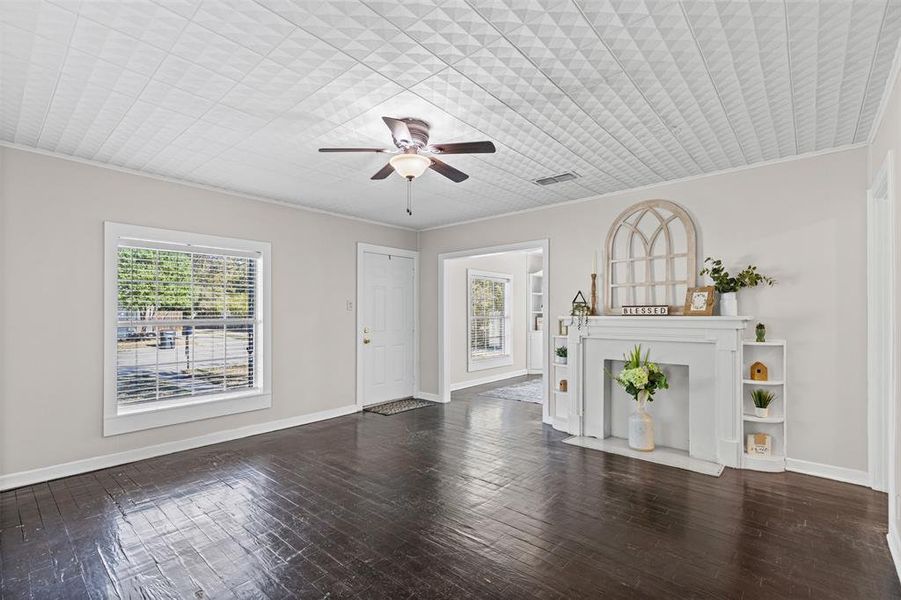 Unfurnished living room with healthy amount of natural light, dark wood-type flooring, ceiling fan, and crown molding