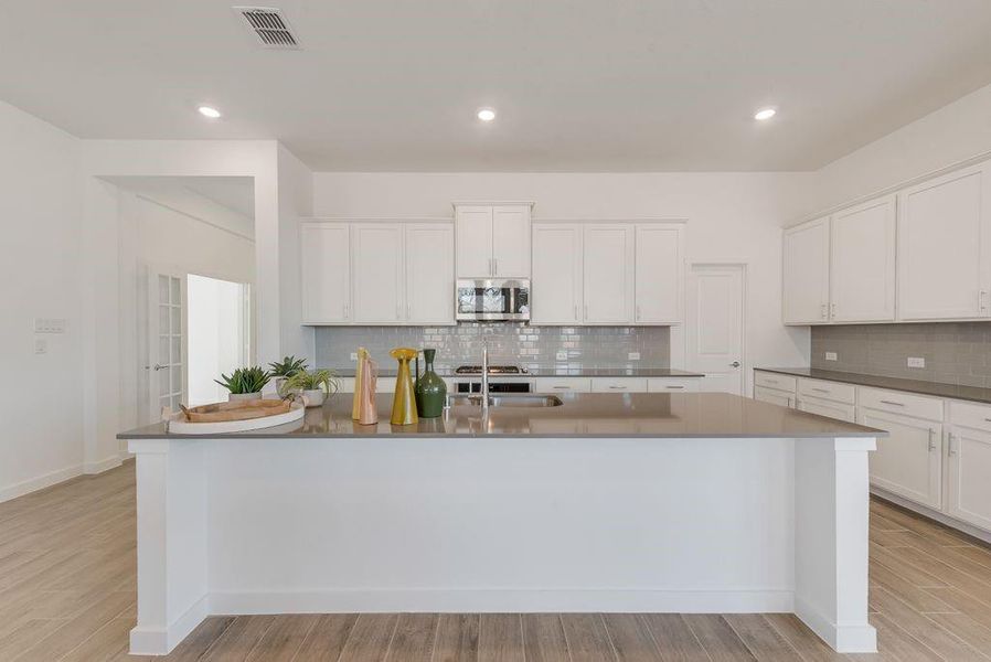 Kitchen featuring stainless steel microwave, tasteful backsplash, white cabinetry, a center island with sink, and recessed lighting