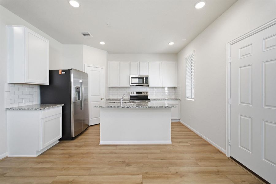 Kitchen featuring white cabinetry, light stone countertops, stainless steel appliances, an island with sink, and light wood-style flooring
