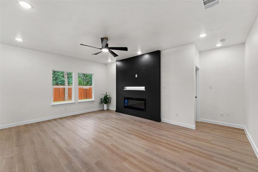 Spacious living area featuring light wood-finish flooring, recessed lighting, and a modern ceiling fan Spacious living area featuring light wood-finish flooring, recessed lighting, and a modern ceiling fan