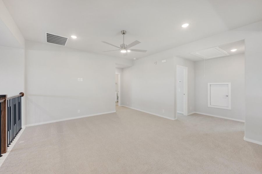 Open upstairs loft with beige carpet, ceiling fan, and staircase railing along the left wall Open upstairs loft with beige carpet, ceiling fan, and staircase railing along the left wall