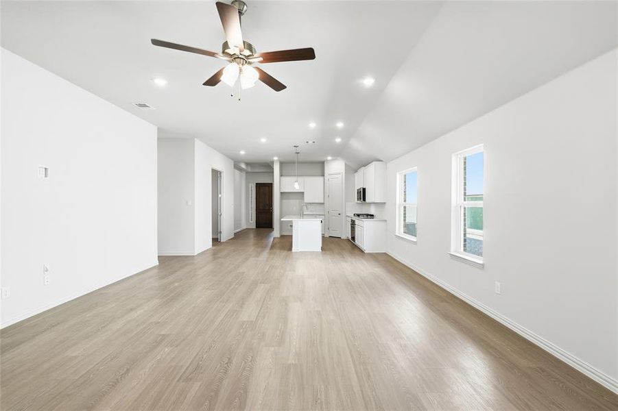 Unfurnished living room featuring light wood finished floors, ceiling fan, vaulted ceiling, and recessed lighting
