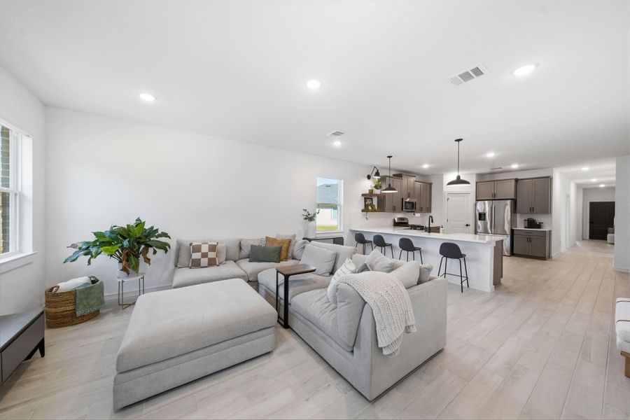 This photo showcases a bright, open-concept living space combining a modern kitchen and cozy living area. The kitchen features sleek cabinetry, stainless steel appliances, and a large island with bar seating. Adjacent is a spacious, comfortable seating area with neutral tones and natural light.