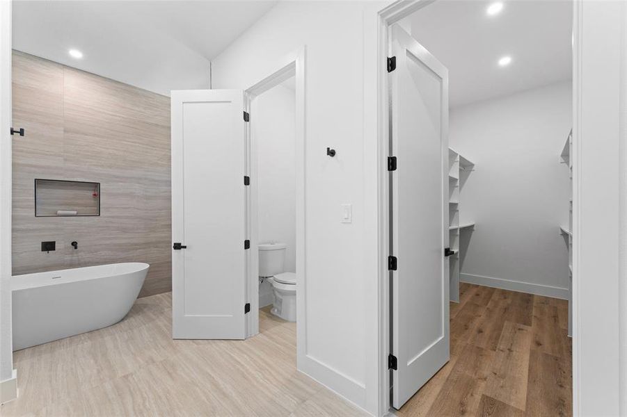 Bathroom featuring a freestanding bath, recessed lighting, tile walls, a walk in closet, and light wood finished floors
