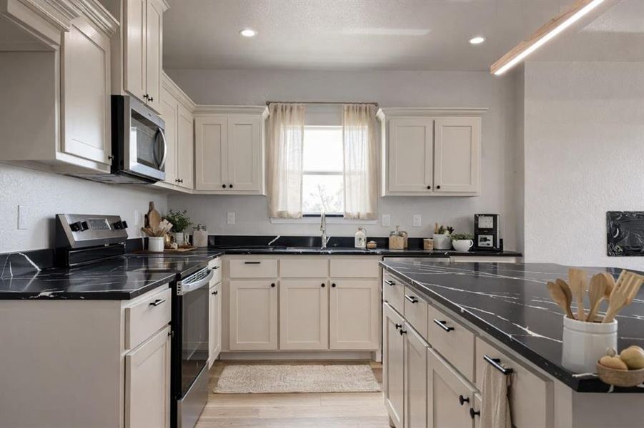 Kitchen featuring stainless steel appliances, recessed lighting, light wood-style floors, and dark stone countertops