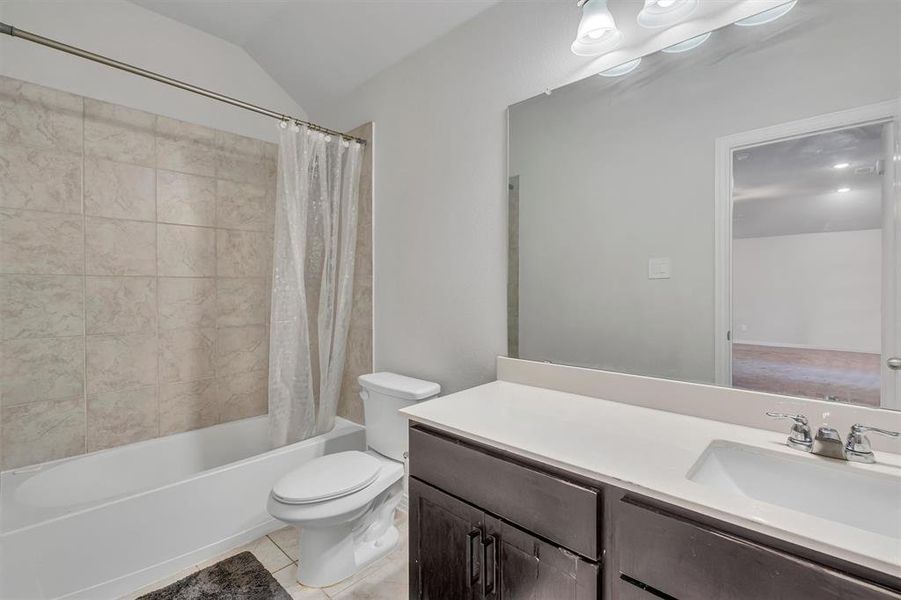 Full bathroom with shower / tub combo with curtain, vanity, toilet, lofted ceiling, and tile patterned flooring