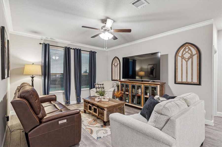 Living area featuring ceiling fan, light wood finished floors, and crown molding Living area featuring ceiling fan, light wood finished floors, and crown molding