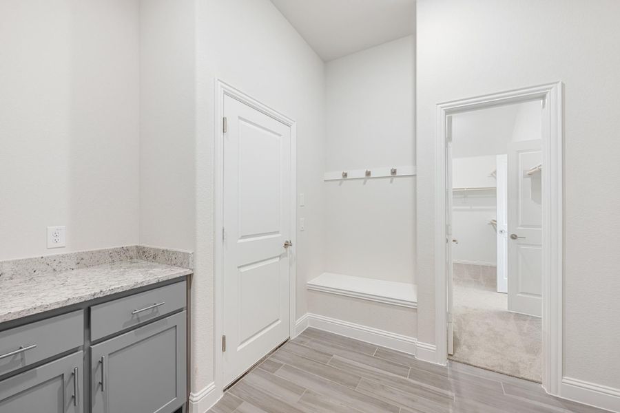 Mudroom with built-in bench, coat hooks, gray cabinets with granite countertop, and wood-look tile floors Mudroom with built-in bench, coat hooks, gray cabinets with granite countertop, and wood-look tile floors