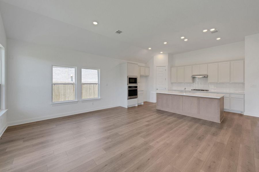 Kitchen with vaulted ceiling, decorative backsplash, recessed lighting, light countertops, and oven