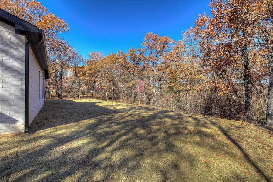 Back yard has retaining wall and surrounding trees for shade.
