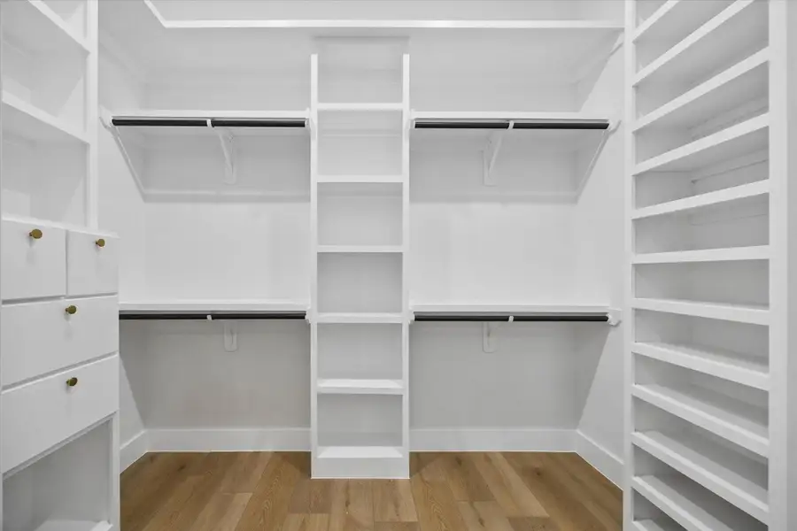 This is a spacious, modern walk-in closet featuring white shelving, hanging rods, and a ladder for upper storage access. The wooden floor adds warmth to the clean, bright design. This is a spacious, modern walk-in closet featuring white shelving, hanging rods, and a ladder for upper storage access. The wooden floor adds warmth to the clean, bright design.