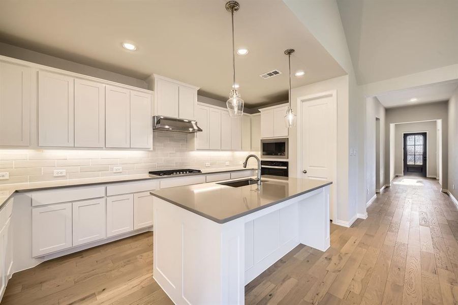 Kitchen featuring sink, light hardwood / wood-style flooring, an island with sink, white cabinetry, and stainless steel appliances