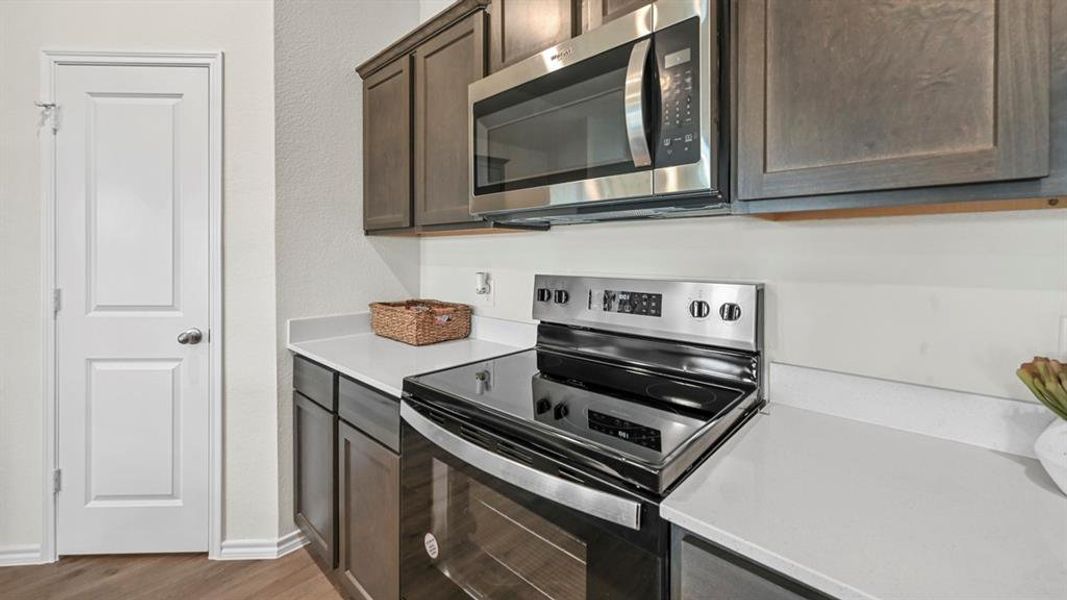 Kitchen featuring appliances with stainless steel finishes, dark brown cabinetry, dark wood-type flooring, and light stone countertops Kitchen featuring appliances with stainless steel finishes, dark brown cabinetry, dark wood-type flooring, and light stone countertops