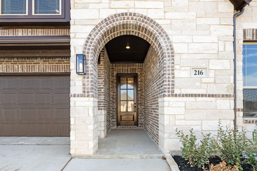 Home entrance with brick arched entryway, wood and glass front door, and stone exterior facade