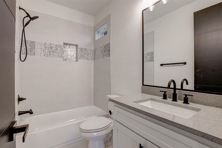 Full bathroom featuring vanity, tiled shower / bath combo, and toilet