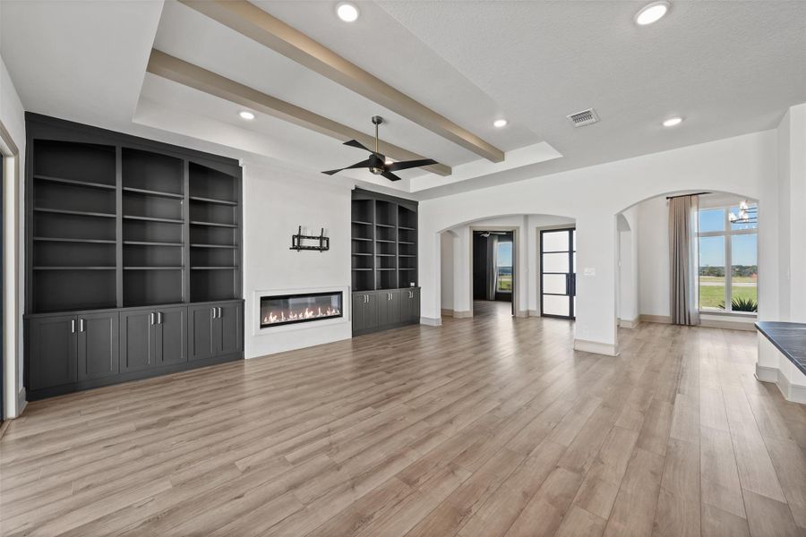 Unfurnished living room with light wood finished floors, visible vents, ceiling fan, a tray ceiling, and arched walkways