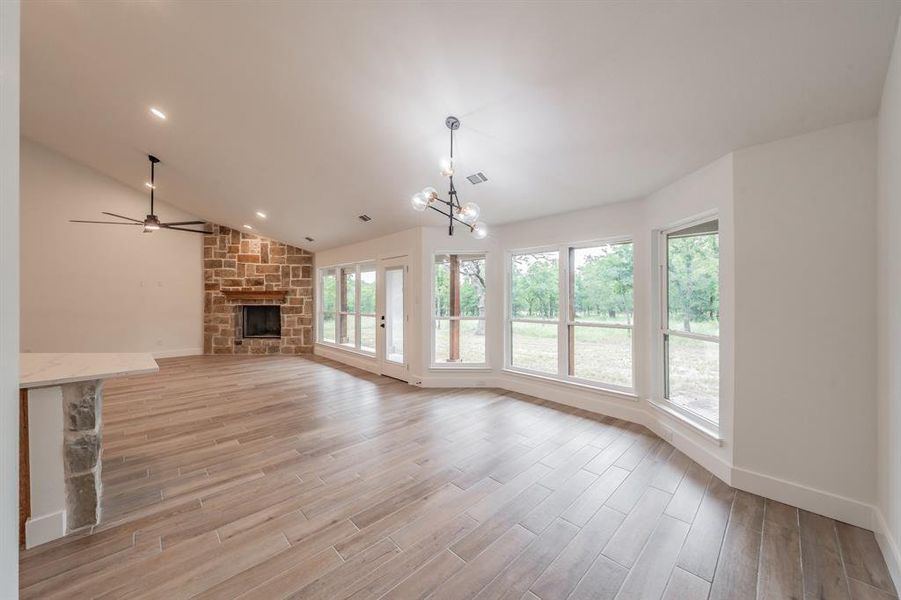 Unfurnished living room featuring a fireplace, light wood finished floors, a ceiling fan, a chandelier, and vaulted ceiling