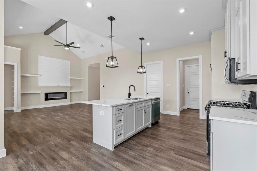 Kitchen featuring appliances with stainless steel finishes, light stone counters, decorative light fixtures, white cabinets, and an island with sink