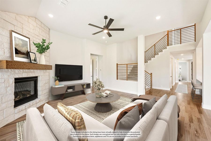 Open living room with stone fireplace, hardwood floors, ceiling fan, and staircase with modern railing Open living room with stone fireplace, hardwood floors, ceiling fan, and staircase with modern railing