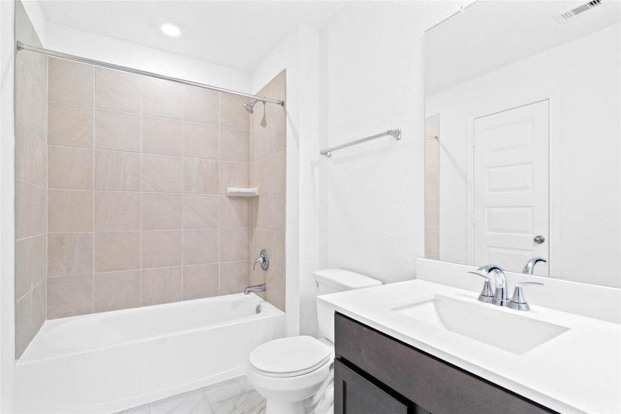 The secondary bathroom showcases tile flooring, a bath/shower combo with Daltile tile surround, a vanity with knee space, a stunning light countertop, a stylish mirror, sleek fixtures, and contemporary finishes throughout.