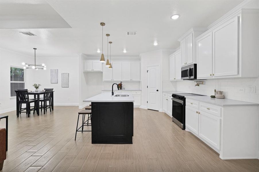 Kitchen with a center island with sink, white cabinets, stainless steel appliances, and decorative light fixtures