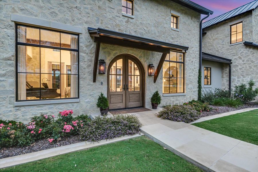 Exterior entry at dusk with french doors, a yard, stone siding, and stucco siding Exterior entry at dusk with french doors, a yard, stone siding, and stucco siding