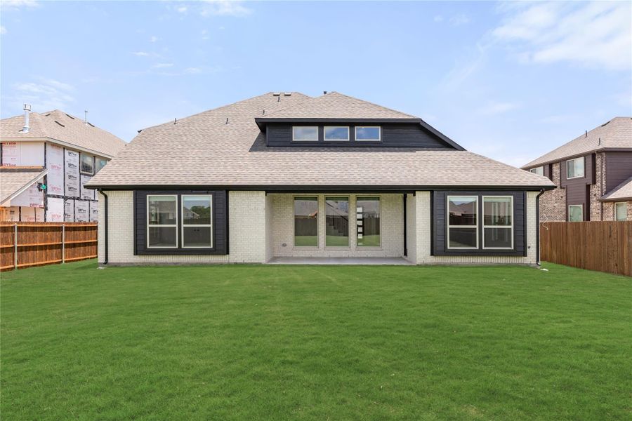 Rear exterior of single-story brick home with dark trim, large windows, patio doors, and fenced backyard with green lawn.