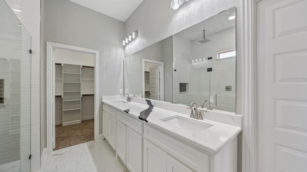 Bathroom featuring double vanity, marble finish floor, a spacious closet, a shower stall, and a sink