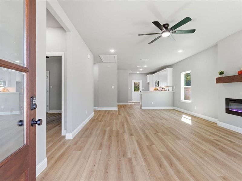 Unfurnished living room featuring attic access, light wood-style floors, ceiling fan, a glass covered fireplace, and recessed lighting Unfurnished living room featuring attic access, light wood-style floors, ceiling fan, a glass covered fireplace, and recessed lighting