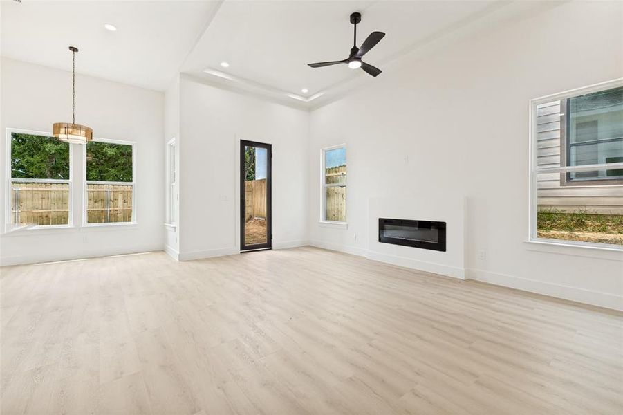 Spacious interior featuring high vaulted ceilings, modern wood-finish flooring, an integrated electric fireplace, multiple large windows, and a contemporary ceiling fan Spacious interior featuring high vaulted ceilings, modern wood-finish flooring, an integrated electric fireplace, multiple large windows, and a contemporary ceiling fan