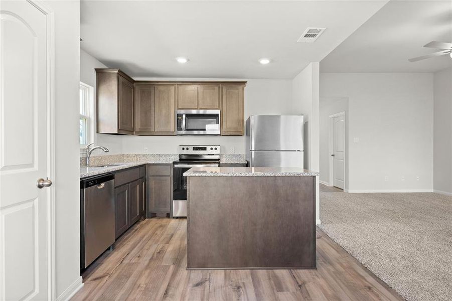 Kitchen featuring stainless steel appliances, a sink, light stone counters, a center island, and light wood-style floors
