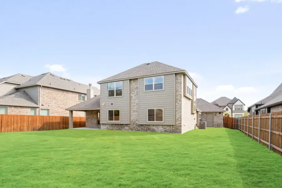 Two-story brick home with tan siding, large backyard, and wood privacy fence