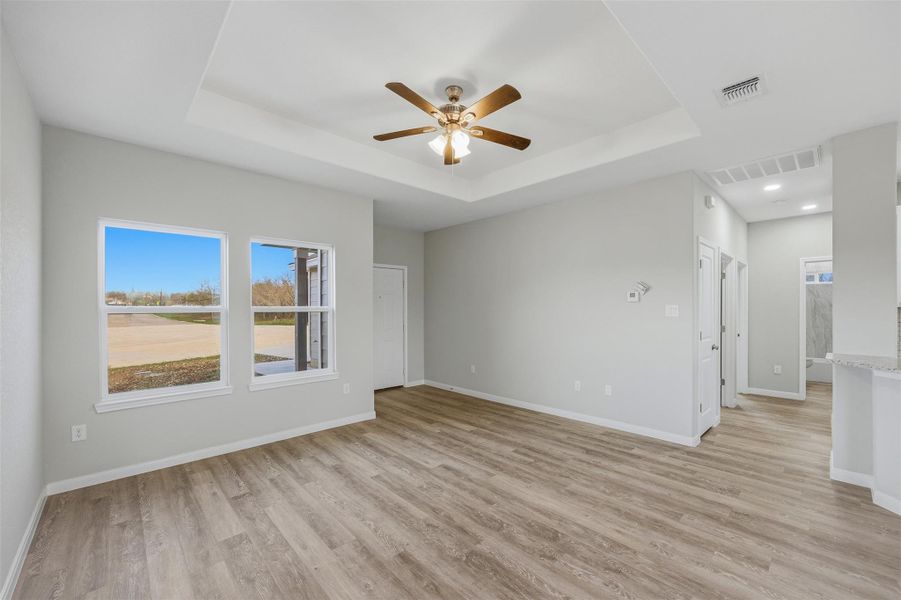 A welcoming living space features light wood flooring, a decorative tray ceiling, and a prominent ceiling fan.