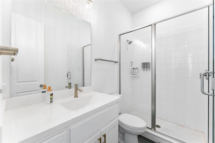 Bathroom featuring a white vanity with a single basin sink, a large mirror, and a glass-enclosed shower with white tiled walls