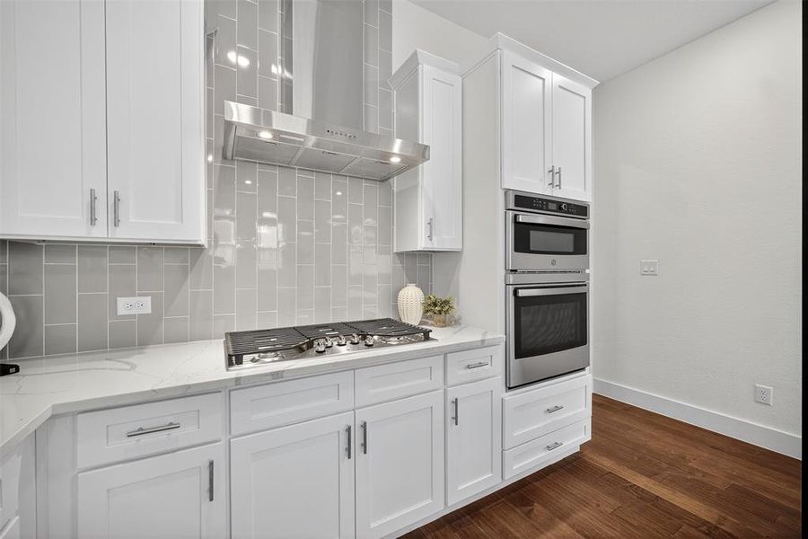 Kitchen featuring wall chimney range hood, backsplash, white cabinetry, stainless steel appliances, and dark wood-style floors