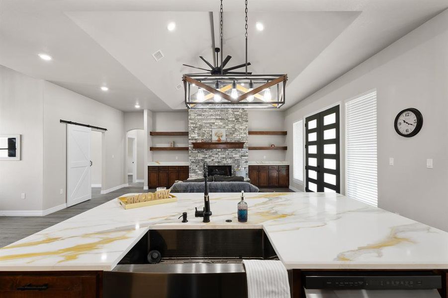 Kitchen with a barn door, open floor plan, a kitchen island with sink, light stone counters, and recessed lighting