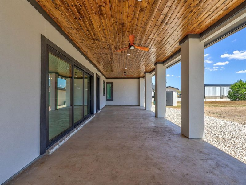 Rich wood plank ceilings shelter a spacious concrete patio anchored by substantial support pillars.