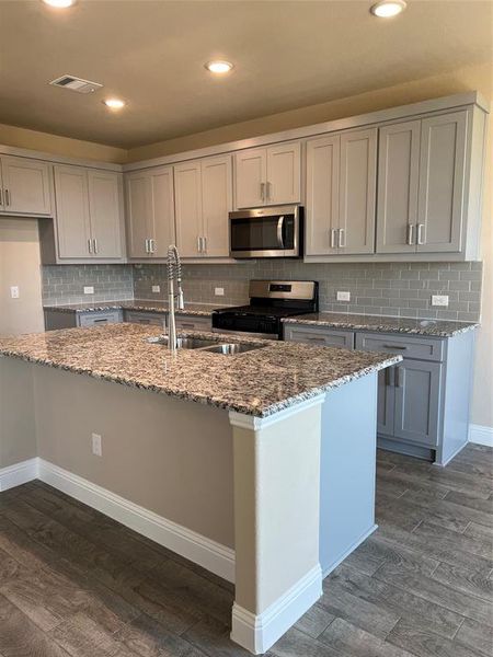 Kitchen featuring stone countertops, a sink, visible vents, dark wood finished floors, and gas range