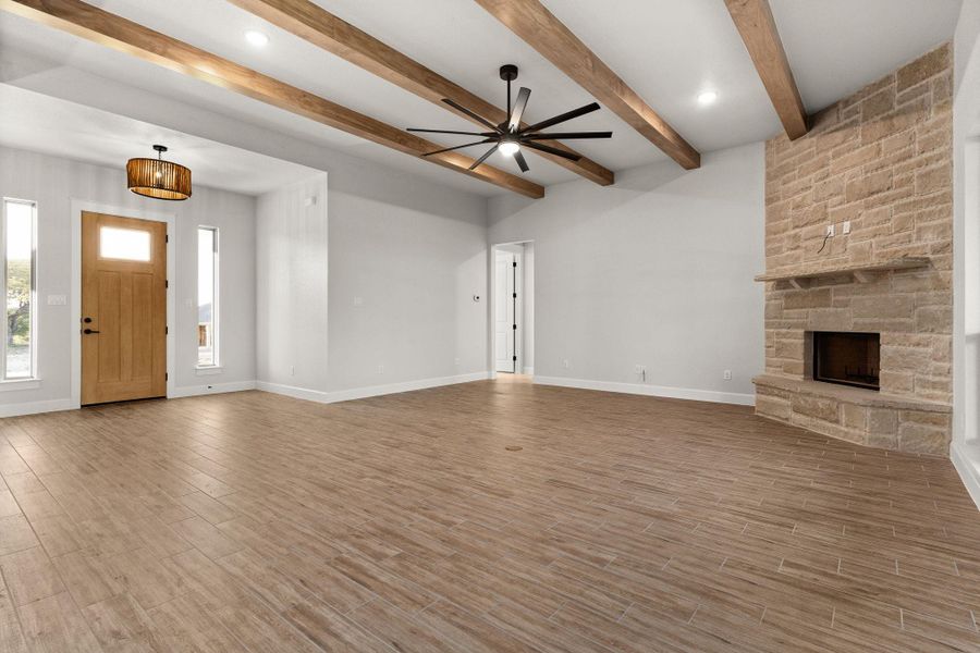 Unfurnished living room with light wood-style flooring, a fireplace, ceiling fan, beam ceiling, and recessed lighting Unfurnished living room with light wood-style flooring, a fireplace, ceiling fan, beam ceiling, and recessed lighting