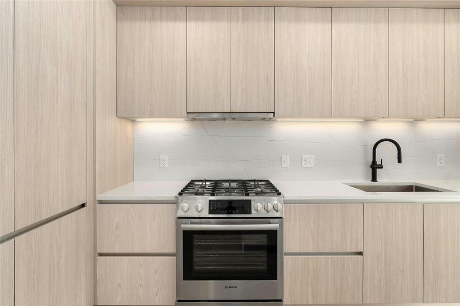 Kitchen with light wood finish cabinetry, stainless steel gas range, modern cabinets, and quartz counters