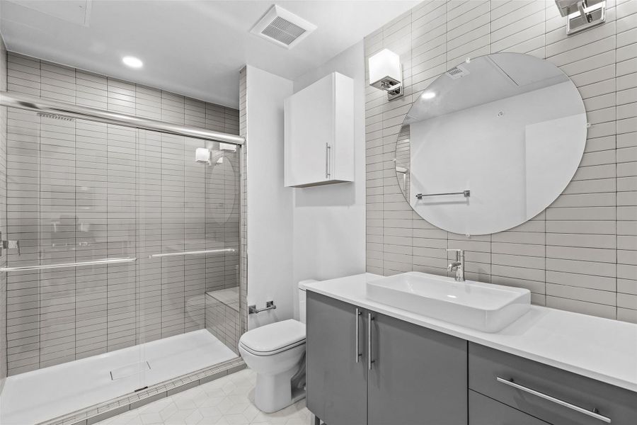 Bathroom with visible vents, toilet, vanity, a stall shower, and tile walls